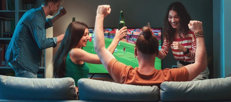 Group of friends cheering in a living room while watching a live football match on television