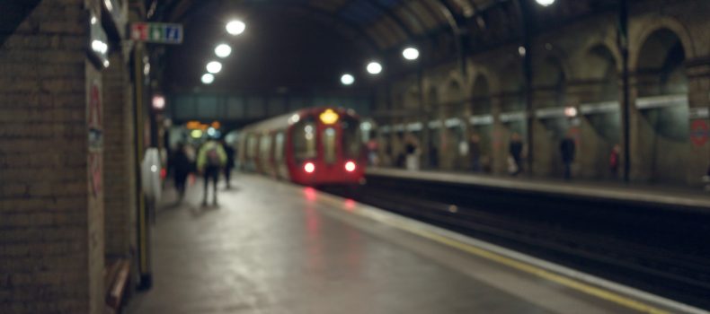 Blurred commuters waiting on a London Underground platform as a red tube train pulls in
